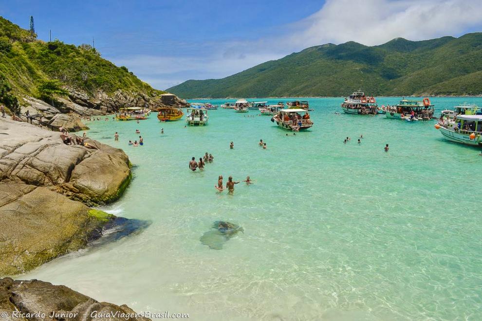 Imagem de vários turistas nas águas cristalinas da Praia do Pontal do Atalaia.